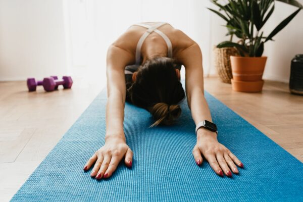 Woman doing a child's pose on a blue yoga mat at home, promoting fitness and wellbeing.